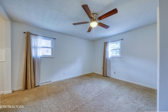 unfurnished room featuring a wealth of natural light, carpet flooring, visible vents, and baseboards