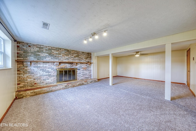 basement featuring a textured ceiling, a fireplace, carpet flooring, visible vents, and baseboards