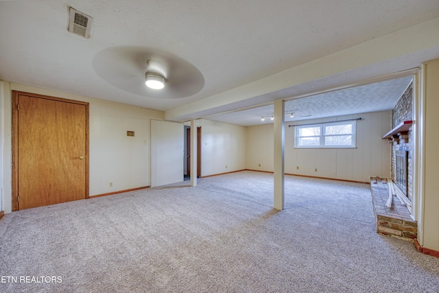 basement featuring a textured ceiling, light colored carpet, visible vents, baseboards, and a brick fireplace