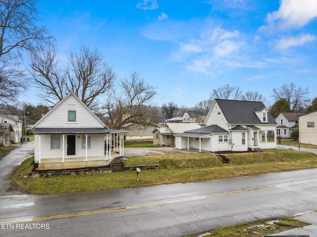 view of front of house with driveway, a residential view, roof with shingles, covered porch, and a front yard