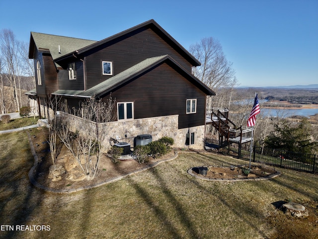 view of side of home with stone siding, central AC, fence, and stairs