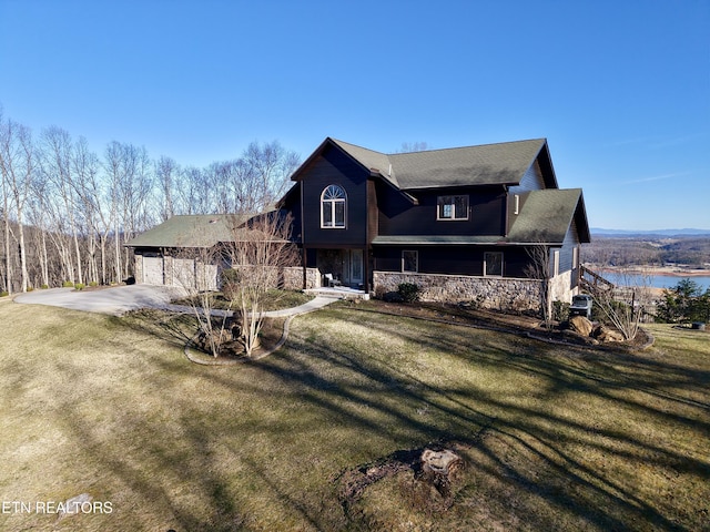 view of front of property featuring covered porch, a water view, driveway, stone siding, and a front yard