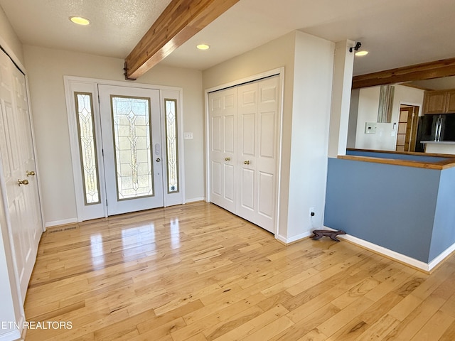 entrance foyer with light wood-type flooring, a wealth of natural light, baseboards, and beam ceiling