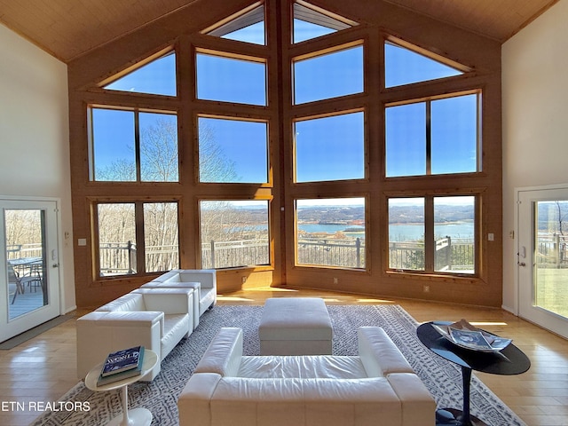 unfurnished living room featuring high vaulted ceiling, a water view, and light wood-style floors