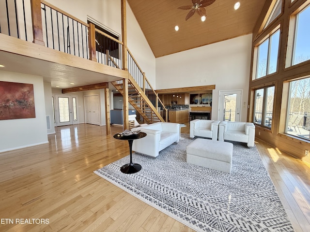 living area with wooden ceiling, hardwood / wood-style flooring, a fireplace, a towering ceiling, and stairs