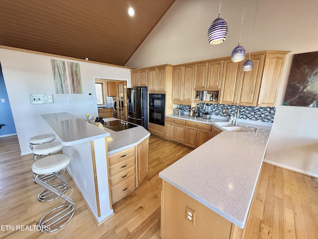 kitchen featuring light wood-style flooring, a kitchen breakfast bar, light countertops, black appliances, and a sink