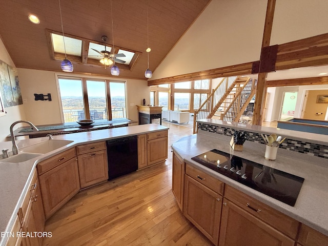 kitchen featuring a skylight, light wood-style flooring, hanging light fixtures, black appliances, and a sink