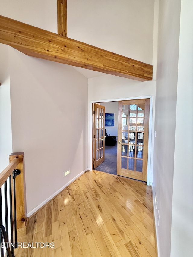 empty room featuring french doors, beamed ceiling, hardwood / wood-style floors, and baseboards