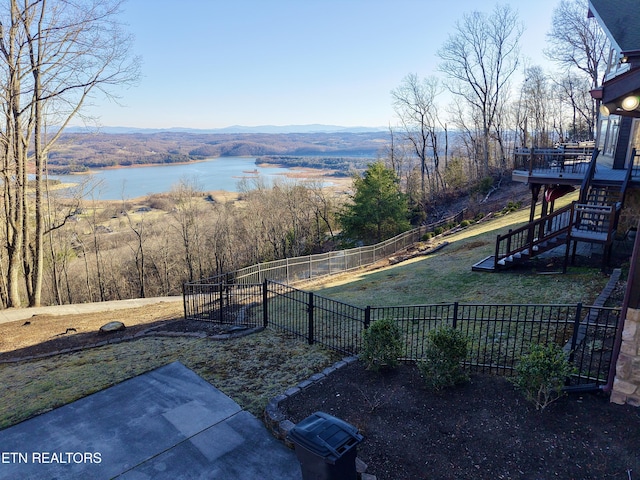 view of yard featuring stairs, a deck with water view, and fence