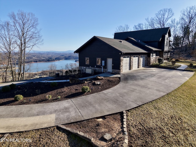 view of home's exterior with a garage, stone siding, a water view, and concrete driveway