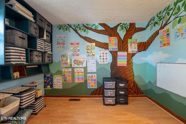 playroom with a textured ceiling, wood finished floors, visible vents, and baseboards