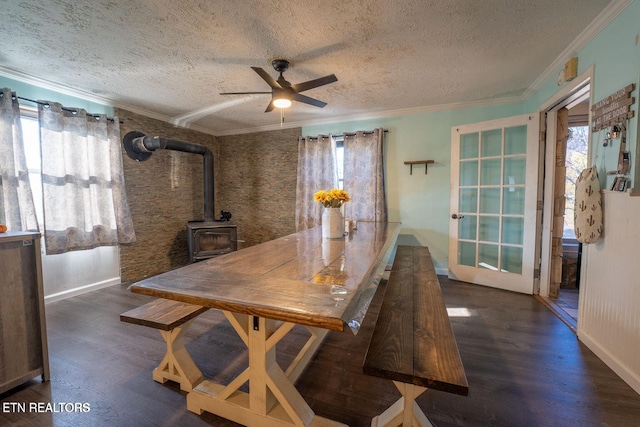 dining area featuring ceiling fan, ornamental molding, wood finished floors, a wood stove, and a textured ceiling