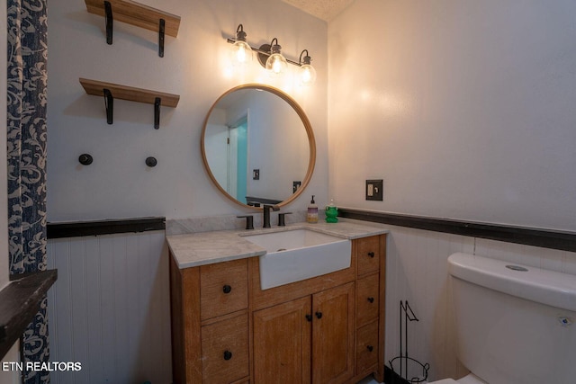 bathroom with a wainscoted wall, vanity, and toilet