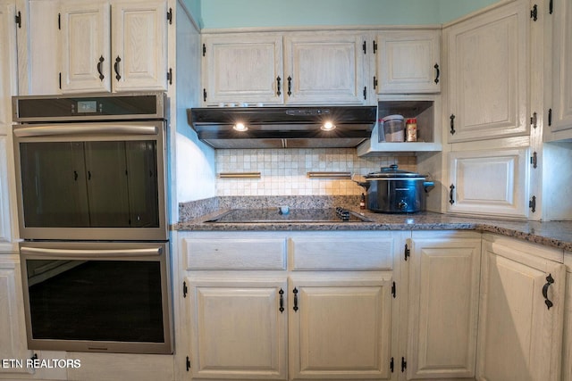 kitchen with stainless steel double oven, stone counters, black electric cooktop, under cabinet range hood, and tasteful backsplash