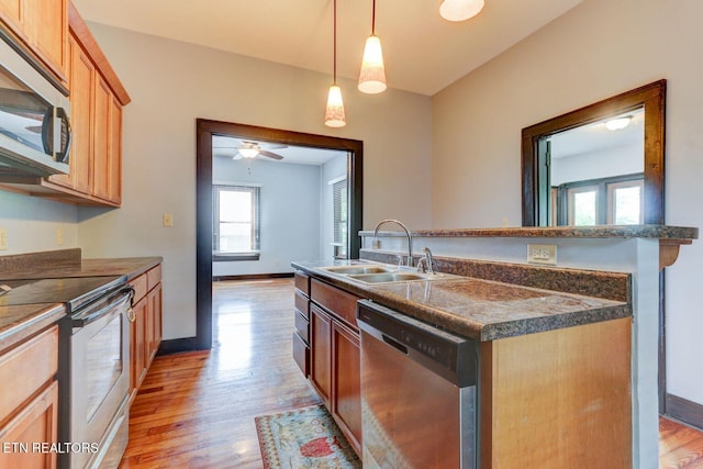 kitchen with a sink, dark countertops, light wood-type flooring, and stainless steel appliances