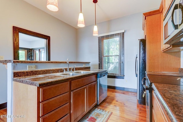 kitchen with a sink, hanging light fixtures, light wood-style floors, appliances with stainless steel finishes, and dark countertops