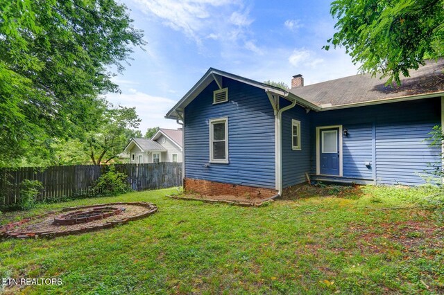 rear view of property with a chimney, a fire pit, a yard, and fence