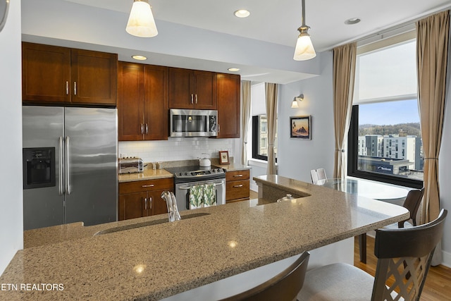 kitchen with light stone countertops, a sink, stainless steel appliances, pendant lighting, and backsplash