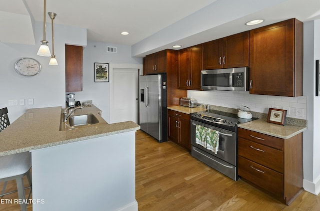 kitchen with visible vents, a peninsula, light wood-style flooring, a sink, and appliances with stainless steel finishes