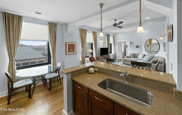 kitchen with pendant lighting, a sink, open floor plan, light wood-style floors, and light stone countertops