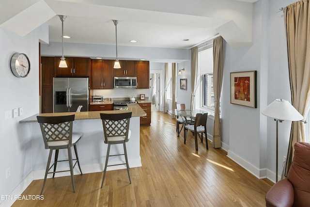 kitchen featuring light wood finished floors, a peninsula, appliances with stainless steel finishes, a kitchen breakfast bar, and decorative light fixtures