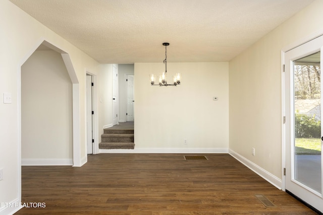 unfurnished dining area with baseboards, visible vents, dark wood-type flooring, a textured ceiling, and a chandelier