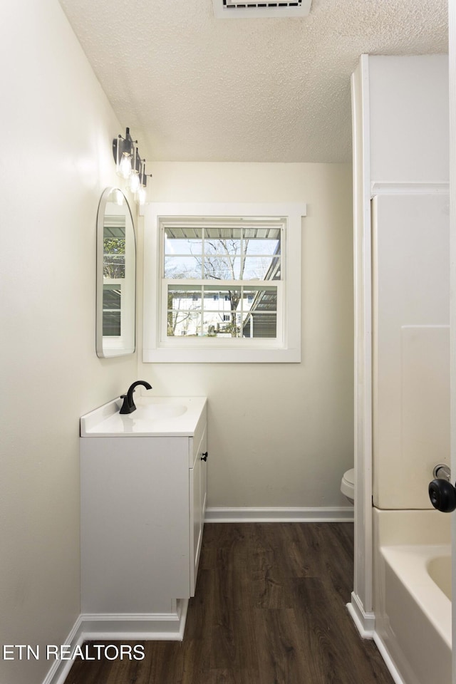 full bath with toilet, a textured ceiling, vanity, wood finished floors, and baseboards