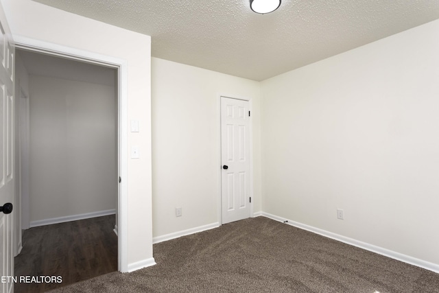 unfurnished bedroom with a textured ceiling, dark carpet, and baseboards