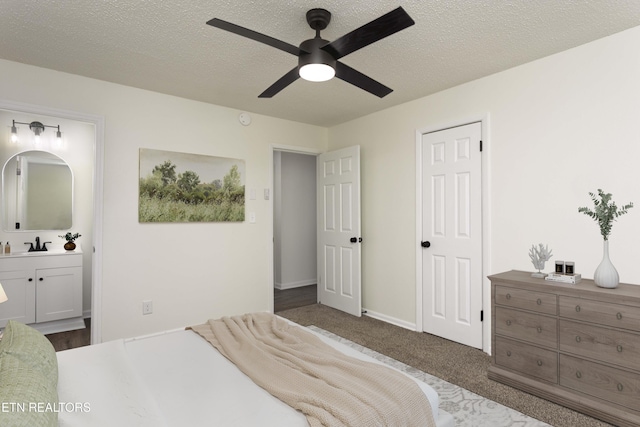 bedroom featuring a sink, dark carpet, a textured ceiling, and ensuite bath