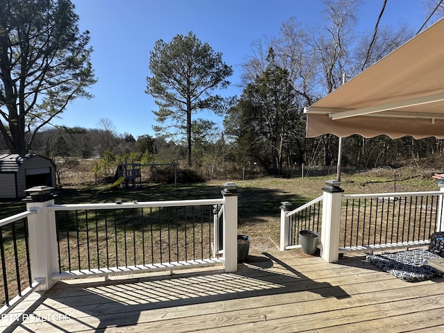 wooden terrace featuring a lawn, a playground, and an outbuilding