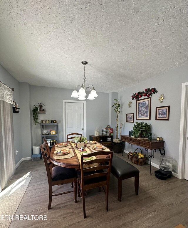 dining room featuring a chandelier, a textured ceiling, baseboards, and wood finished floors