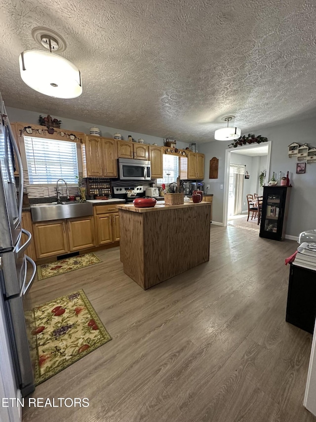 kitchen with light wood finished floors, a kitchen island, stainless steel appliances, and a sink