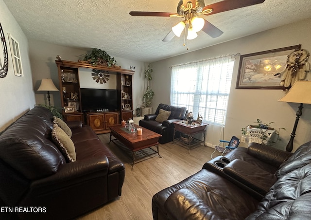 living room with a ceiling fan, light wood-type flooring, and a textured ceiling