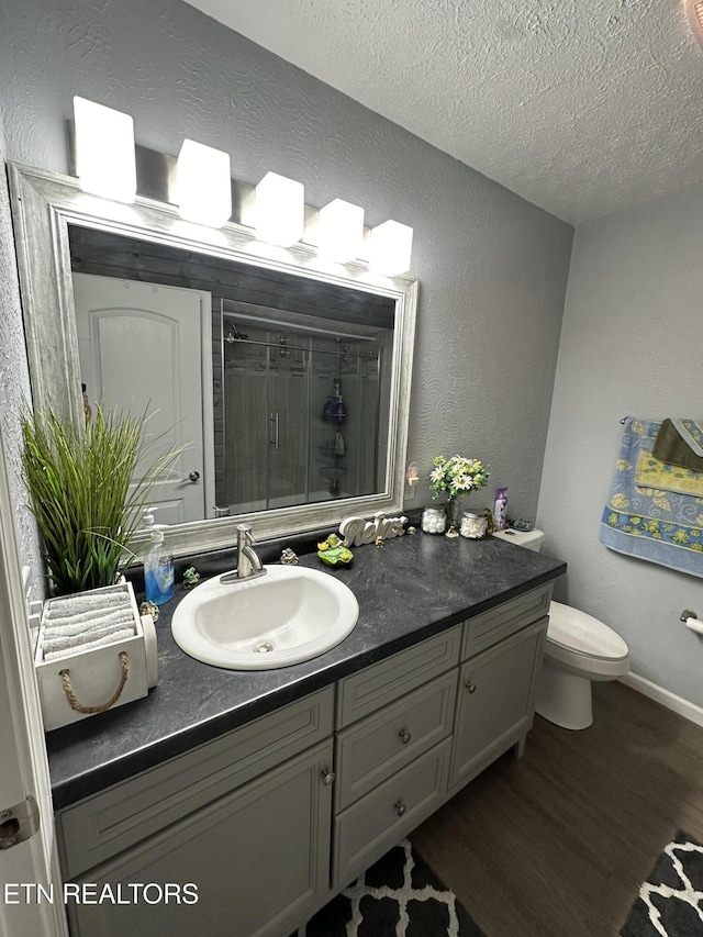 full bath featuring wood finished floors, toilet, a shower stall, a textured ceiling, and vanity