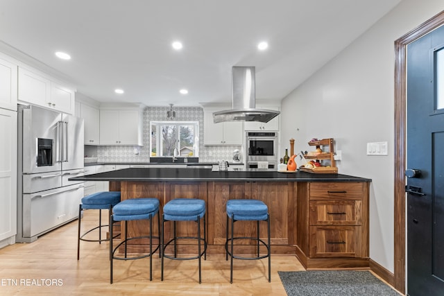 kitchen featuring island exhaust hood, decorative backsplash, appliances with stainless steel finishes, white cabinetry, and a peninsula