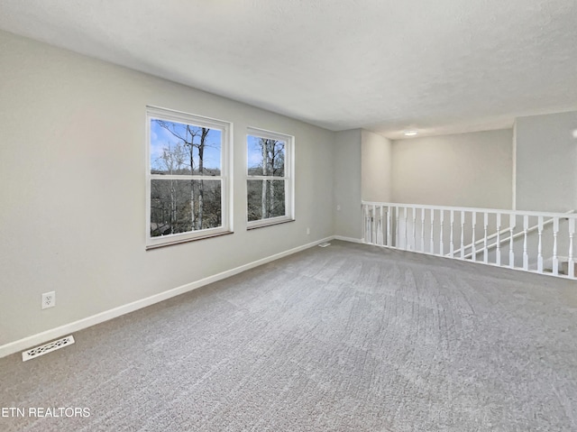 carpeted empty room featuring visible vents, a textured ceiling, and baseboards