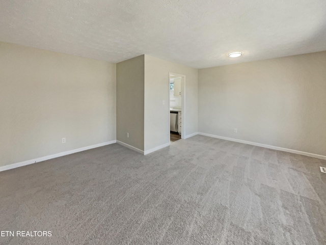 spare room featuring a textured ceiling, carpet floors, and baseboards