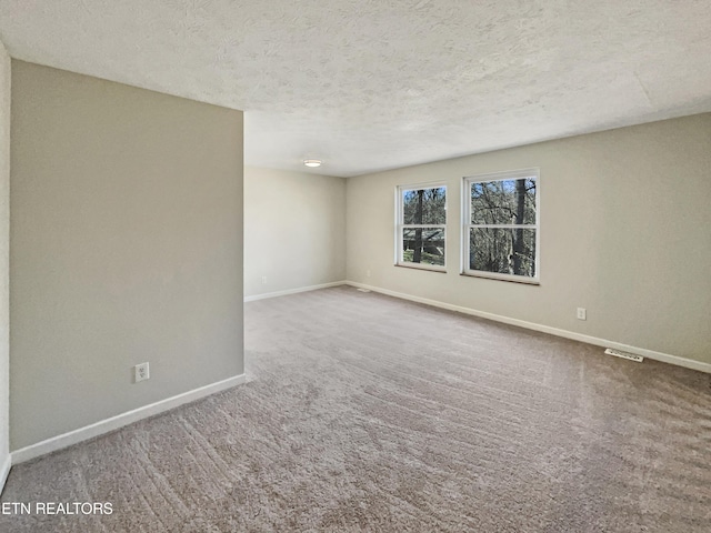 spare room featuring a textured ceiling, carpet, visible vents, and baseboards