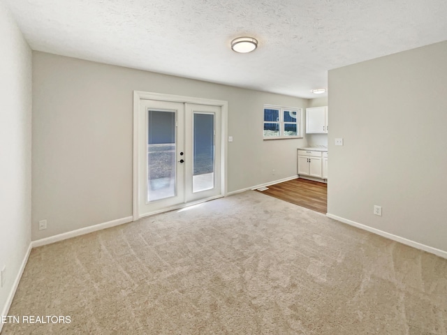 spare room with a textured ceiling, french doors, carpet, and baseboards