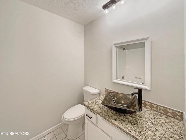 half bathroom featuring a textured ceiling, toilet, vanity, baseboards, and tile patterned floors