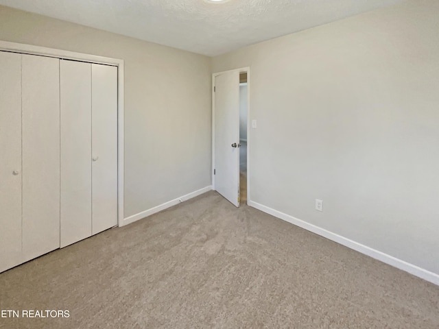 unfurnished bedroom featuring carpet, a textured ceiling, baseboards, and a closet