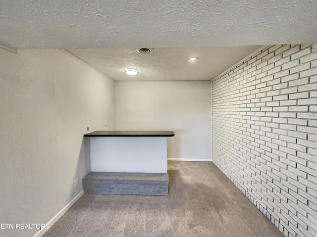 interior space with visible vents, baseboards, brick wall, carpet, and a textured ceiling