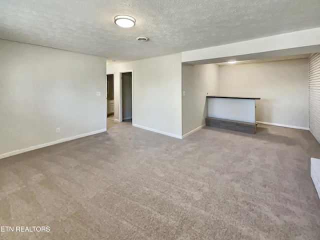 finished basement with a textured ceiling, carpet flooring, visible vents, and baseboards