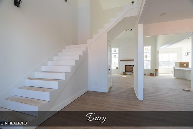 stairs with baseboards, a fireplace, a high ceiling, and wood finished floors