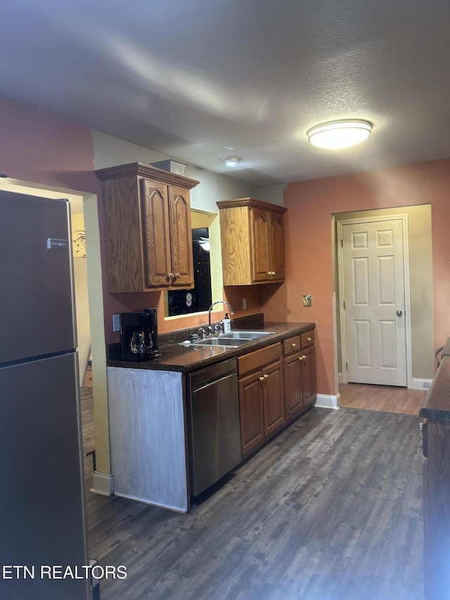 kitchen with dark wood finished floors, dark countertops, stainless steel appliances, and a sink