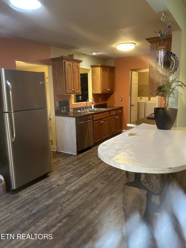 kitchen featuring washing machine and clothes dryer, stainless steel appliances, a sink, dark wood-style flooring, and brown cabinets