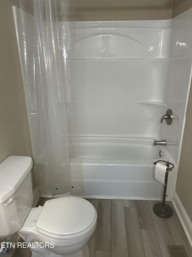 bathroom featuring wood finished floors, visible vents, toilet, baseboards, and shower / tub combo