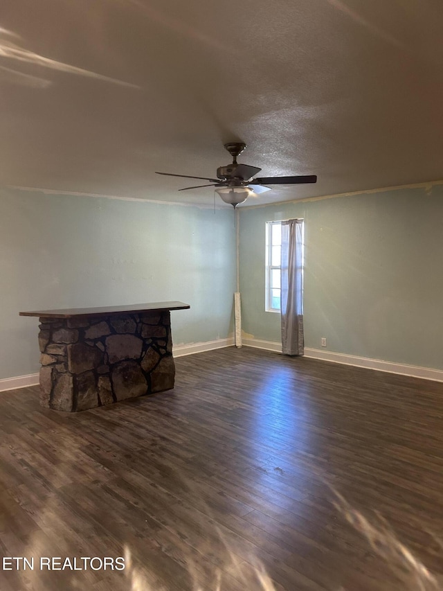 unfurnished living room with a stone fireplace, baseboards, dark wood-type flooring, and ceiling fan