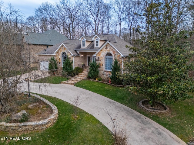 view of front of property with concrete driveway, stone siding, roof with shingles, and a front yard