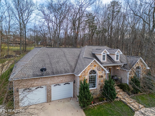 view of front facade with roof with shingles, brick siding, concrete driveway, an attached garage, and stone siding